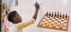 Barn räknar matte på tavla bredvid ett schackbräde. 